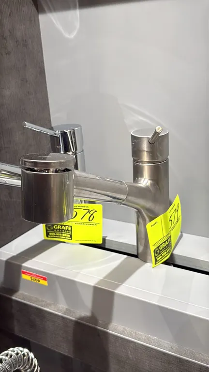 Canadian pull-down kitchen faucet. Features single-lever handle and pull-down spray head. Stainless steel finish. Note: Display stand and adjacent fau