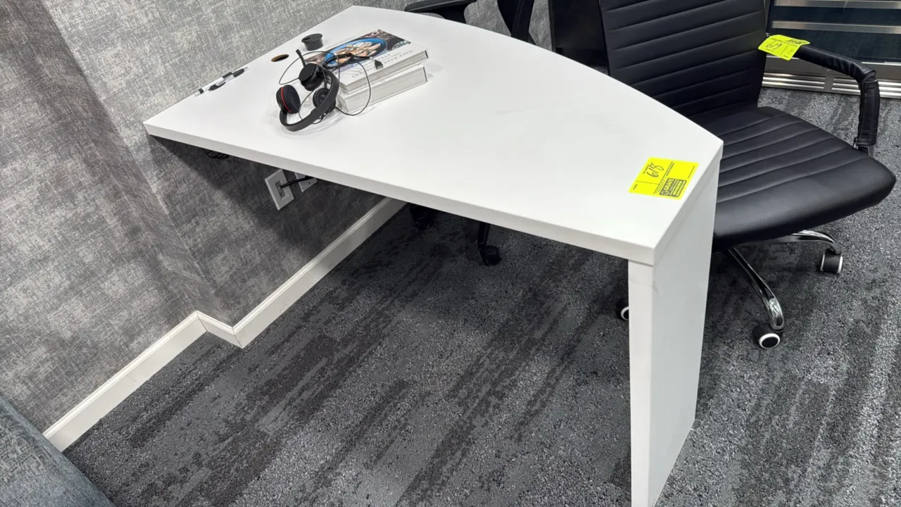 Laminate wall-mounted desk. Features a white finish, curved work surface, and cord management grommet. 51"L. Supported by wall-mount brackets and a si