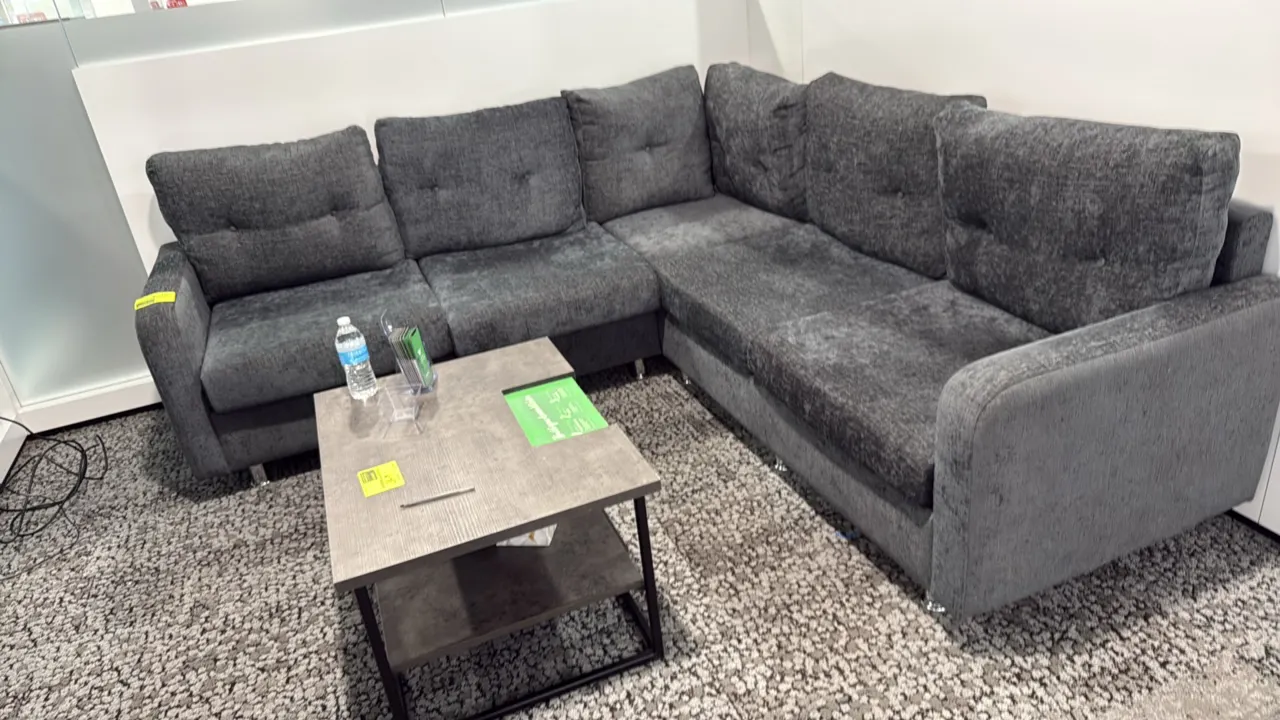 L-shaped sectional couch. Features charcoal gray textured fabric upholstery and tufted back cushions. 87" x 59". Mounted on chrome-tone metal legs. Co