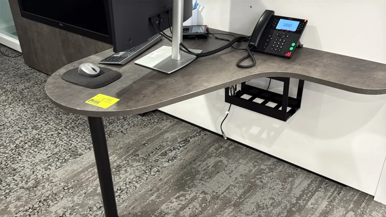 Laminate wall-mounted desk. Features a curved gray woodgrain laminate work surface and an under-desk cable management tray. 42"L. Supported by a black