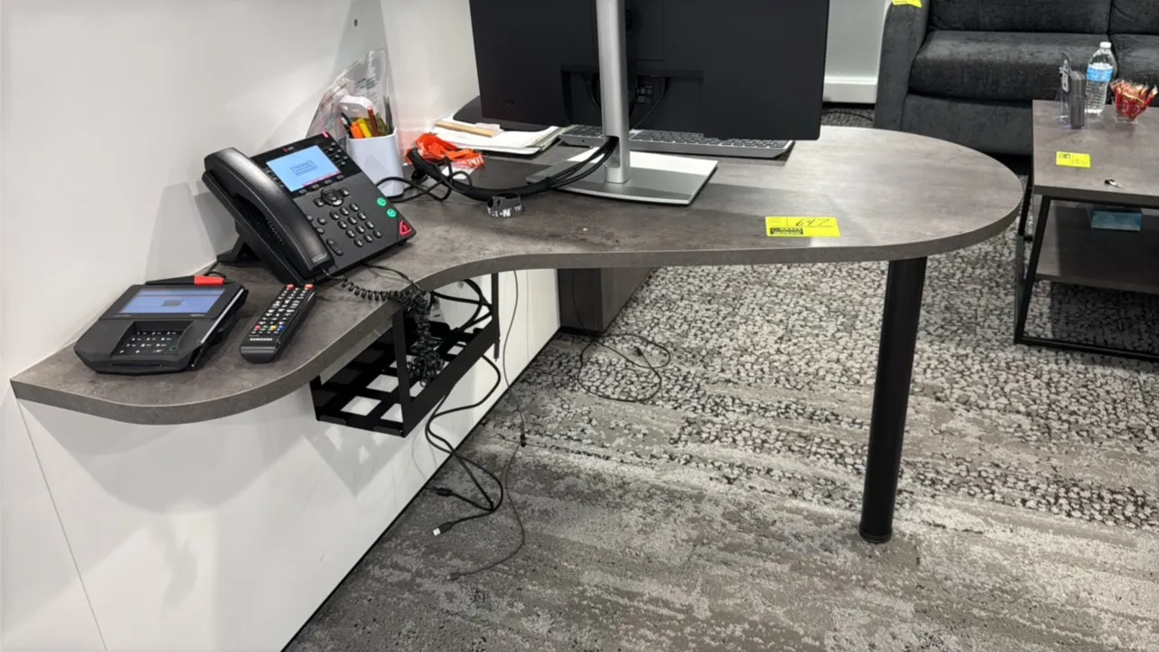 Laminate wall-mounted desk. Features a curved gray laminate top and an under-desk wire cable management tray. 42"L. Supported by a single black metal