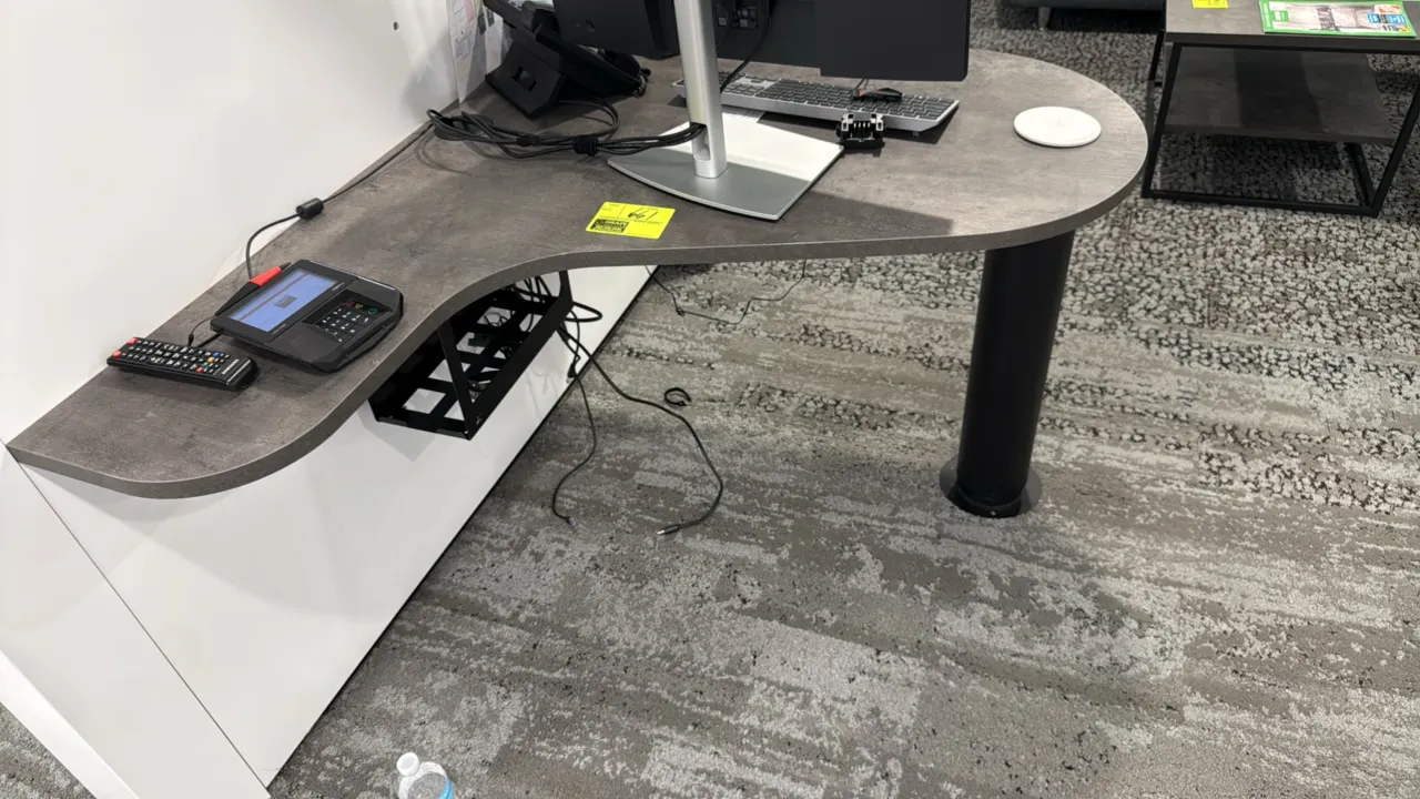 Laminate wall-mounted desk. Features a contoured gray laminate work surface and an undermount wire cable management tray. 42"W. Supported by a black c