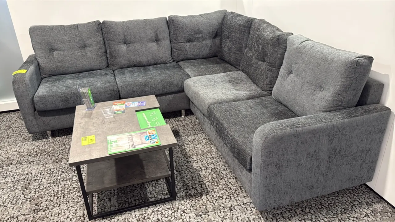 L-shaped sectional couch. Features gray textured fabric upholstery, tufted back cushions, and track arms. 87" x 59". Mounted on chrome-finish metal le