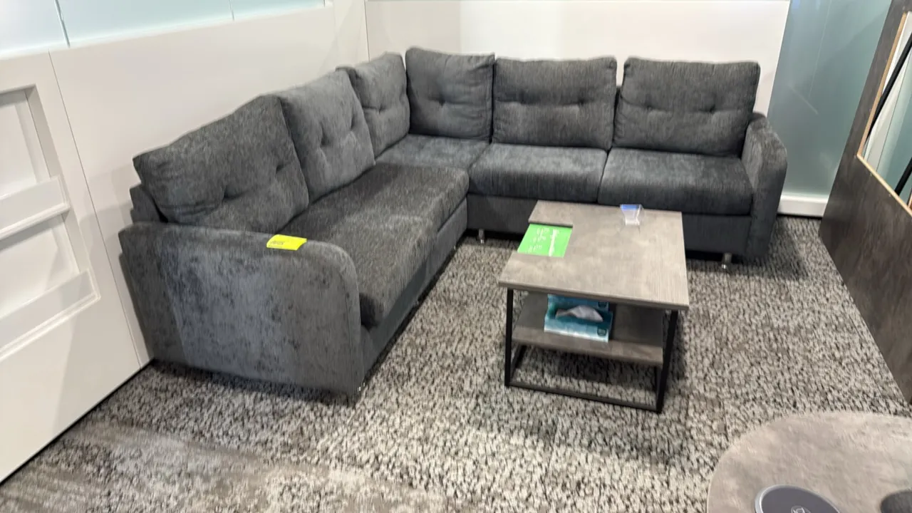 L-shaped sectional couch with coffee table. Couch features gray fabric upholstery with tufted back cushions, measuring 87" x 59". Coffee table feature
