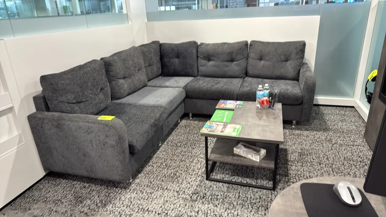 L-shaped sectional couch with coffee table. Couch features gray textured fabric upholstery, tufted back cushions, and chrome-finished legs; measures 8