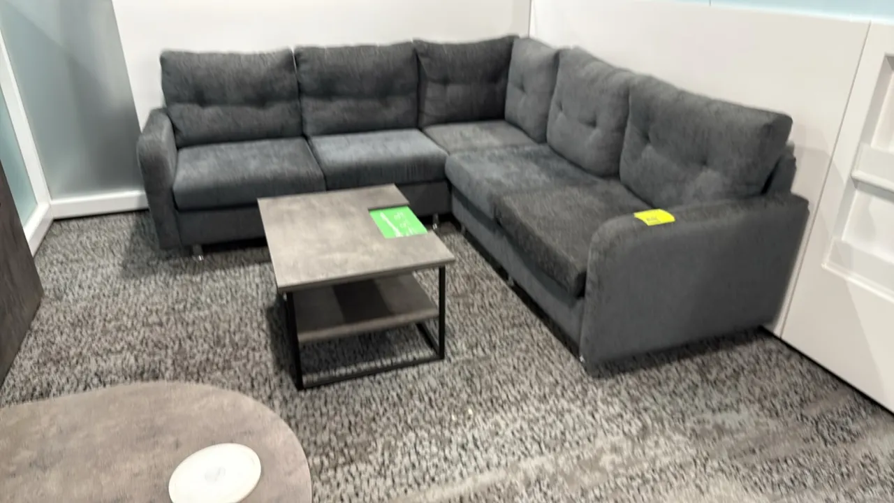 L-shaped sectional couch with coffee table. Couch features gray fabric upholstery, tufted back cushions, and metal legs; measures 87" x 59". Coffee ta