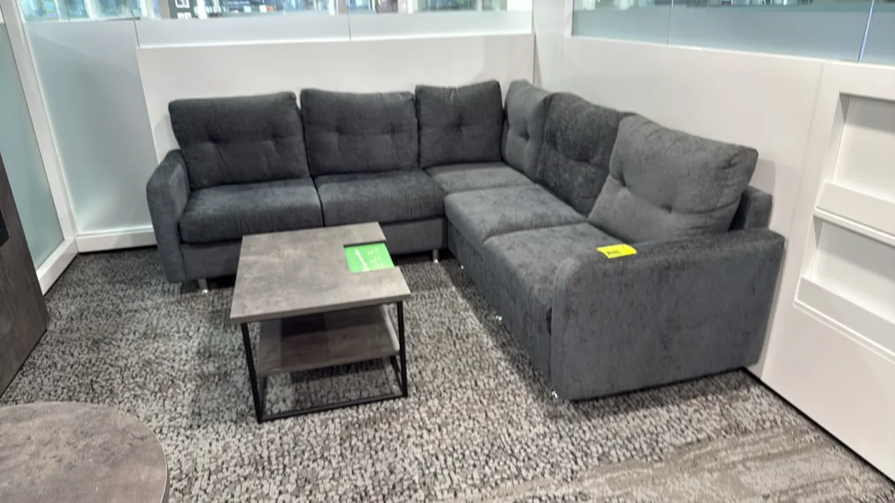 L-shaped sectional sofa and coffee table set. Includes an 87" x 59" gray upholstered sectional sofa featuring tufted back cushions and chrome-tone fee