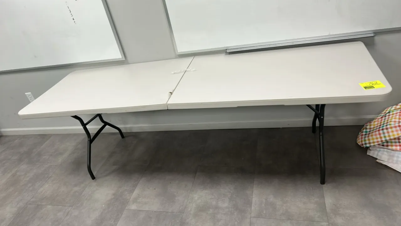 Lifetime collapsible folding table. Features a white polyethylene fold-in-half tabletop and folding metal legs. 8'L.