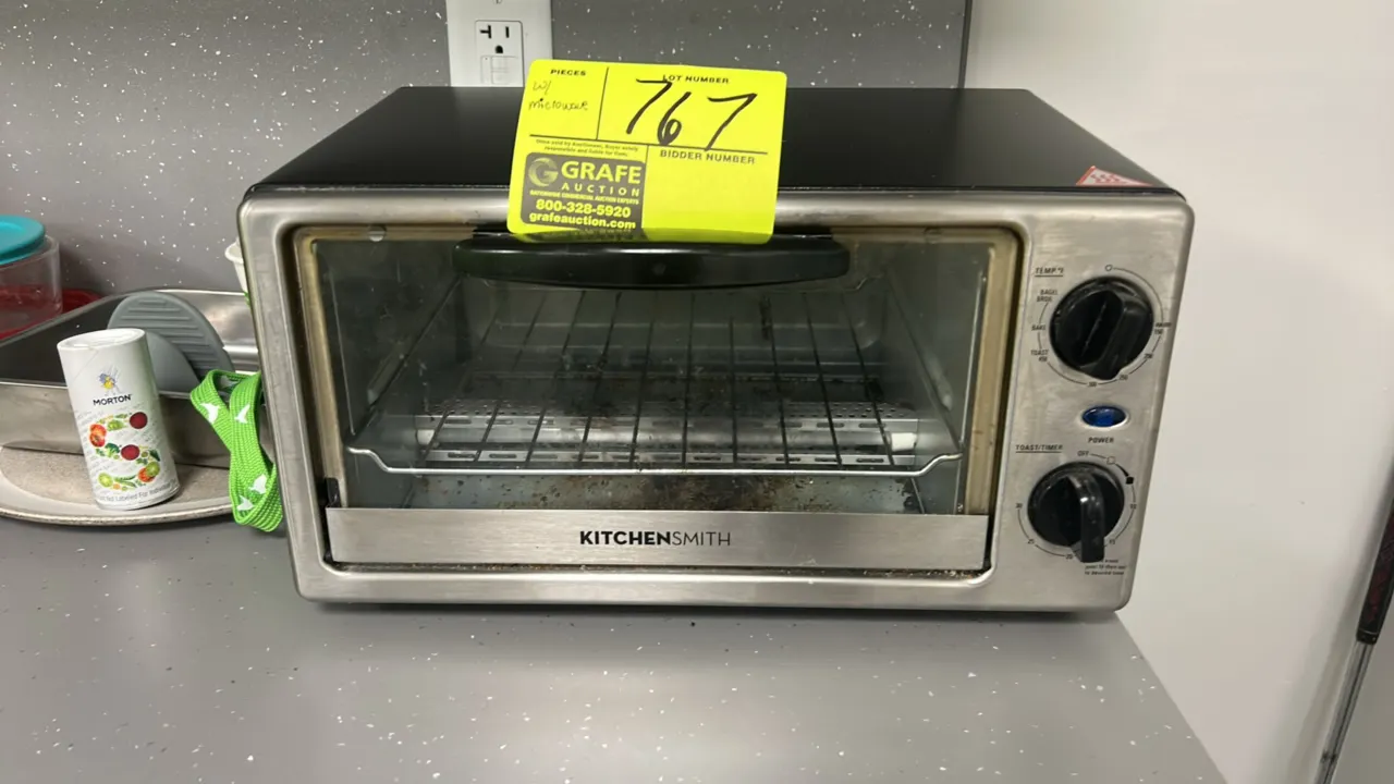 KitchenSmith 4-slice toaster oven. Features stainless steel front trim with black housing, glass door, interior wire rack, and dual dial controls for