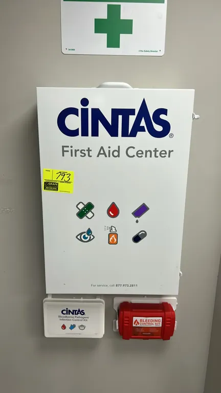 Cintas wall-mounted metal first aid center. Features multi-shelf interior stocked with assorted first aid supplies, interior door pouch organizer, top