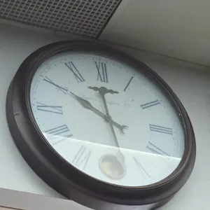 London Timepiece Co. analog wall clock. Features a Roman numeral dial, decorative hands, exposed pendulum, and a dark-finished round frame. 24"Dia.