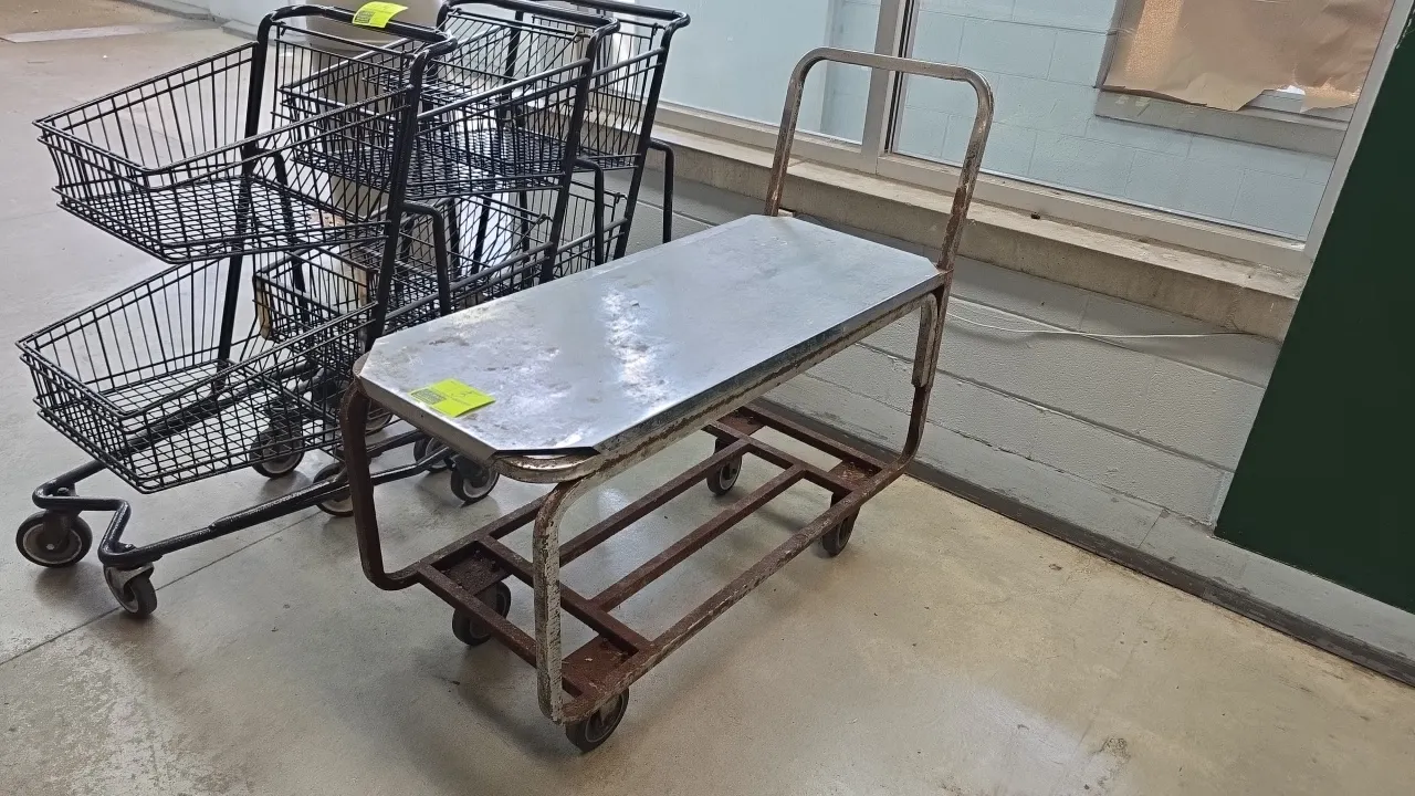 Metal 2-tier stocking cart. Features solid sheet metal upper shelf, open steel lower frame tier, and tubular push handle. 43"L. Mounted on casters. No