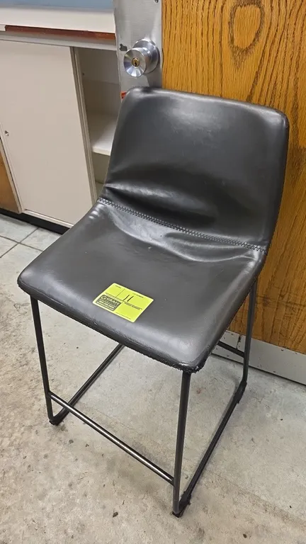 Leather-upholstered bar stool. Features black padded seat and backrest with horizontal seam stitching and an integrated footrest. Mounted on a black m