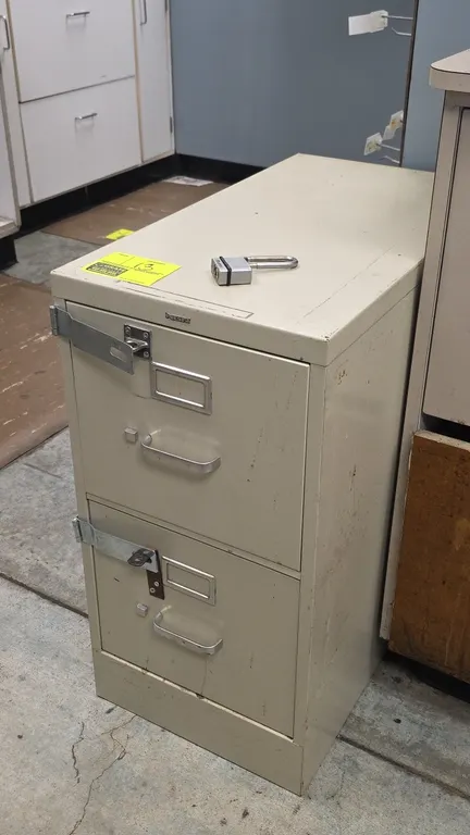 HON 2-drawer vertical filing cabinet. Features metal construction in putty finish, label holders, drawer pull handles, and exterior locking hasps. Inc