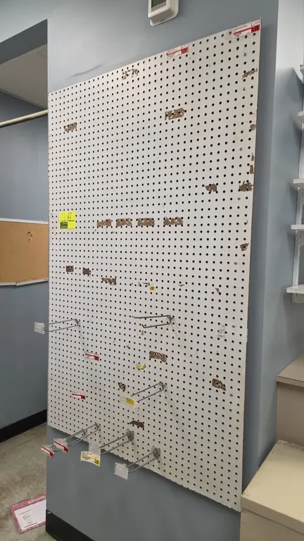 Wall-mounted pegboard display panel. Features white finish and perforated surface. Includes assorted wire display hooks with tag holders. 48" x 60".
