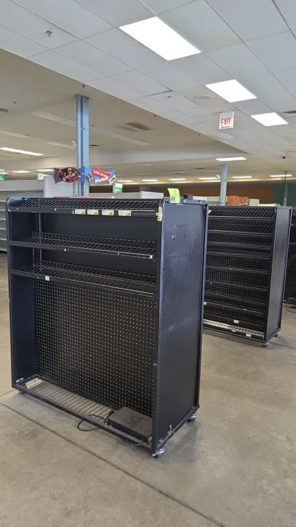 Portable metal candy and magazine merchandisers. Features black metal frames, slanted wire display shelves, lower pegboard display panels, and bottom