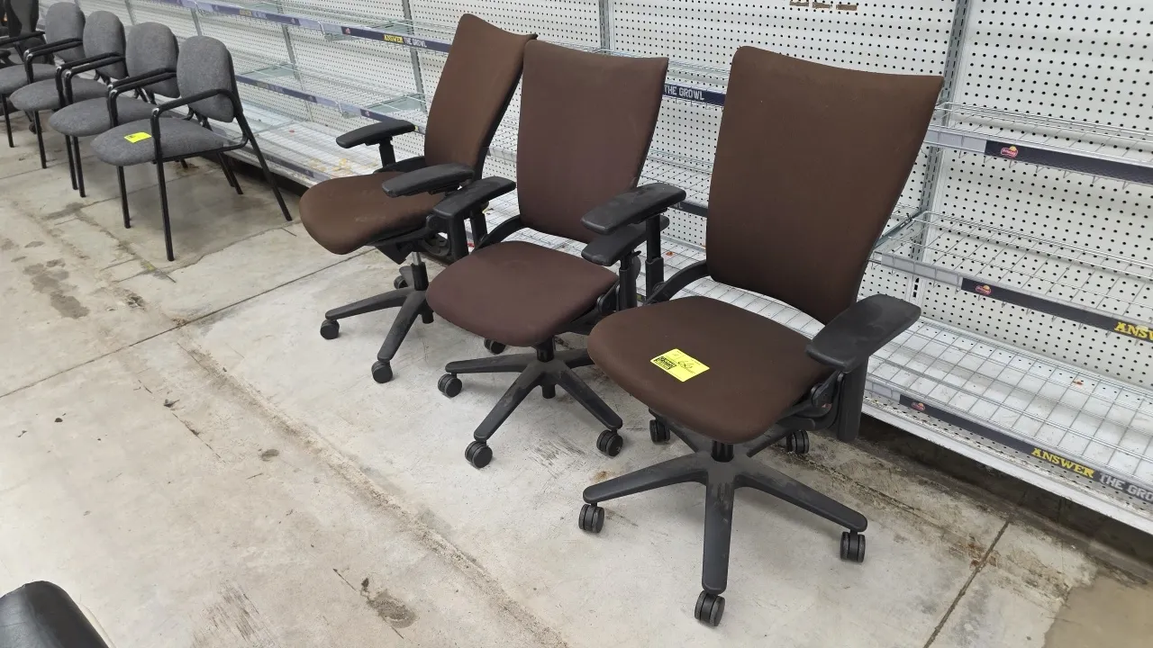 Cushioned adjustable office task chairs. Features brown fabric upholstery, cushioned seats and backs, and adjustable armrests. Mounted on black compos
