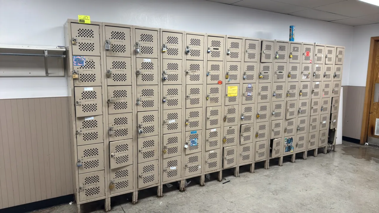 Six-tier metal box locker sections. Features diamond-perforated ventilated doors, integrated label plate holders, and padlock hasps. Tan painted finis