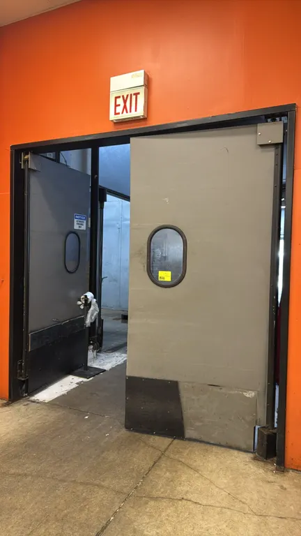 Poly swing doors. Features oval vision panels, lower kick plates, and pivot hinge mounting hardware. Measures 4' x 8'. Bag dispenser stand in foregrou