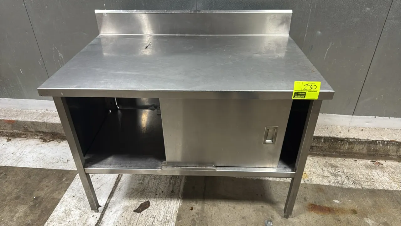 Stainless steel cabinet work table with backsplash. Features stainless steel construction, integrated rear backsplash, and enclosed base cabinet with