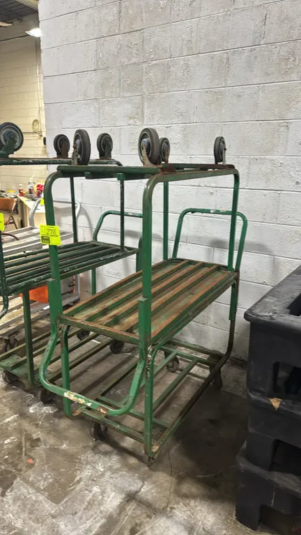 Metal 2-tier carts. Features green tubular metal frame, slatted metal shelves, integrated push handles, and top-mounted casters. 44" x 18". Mounted on