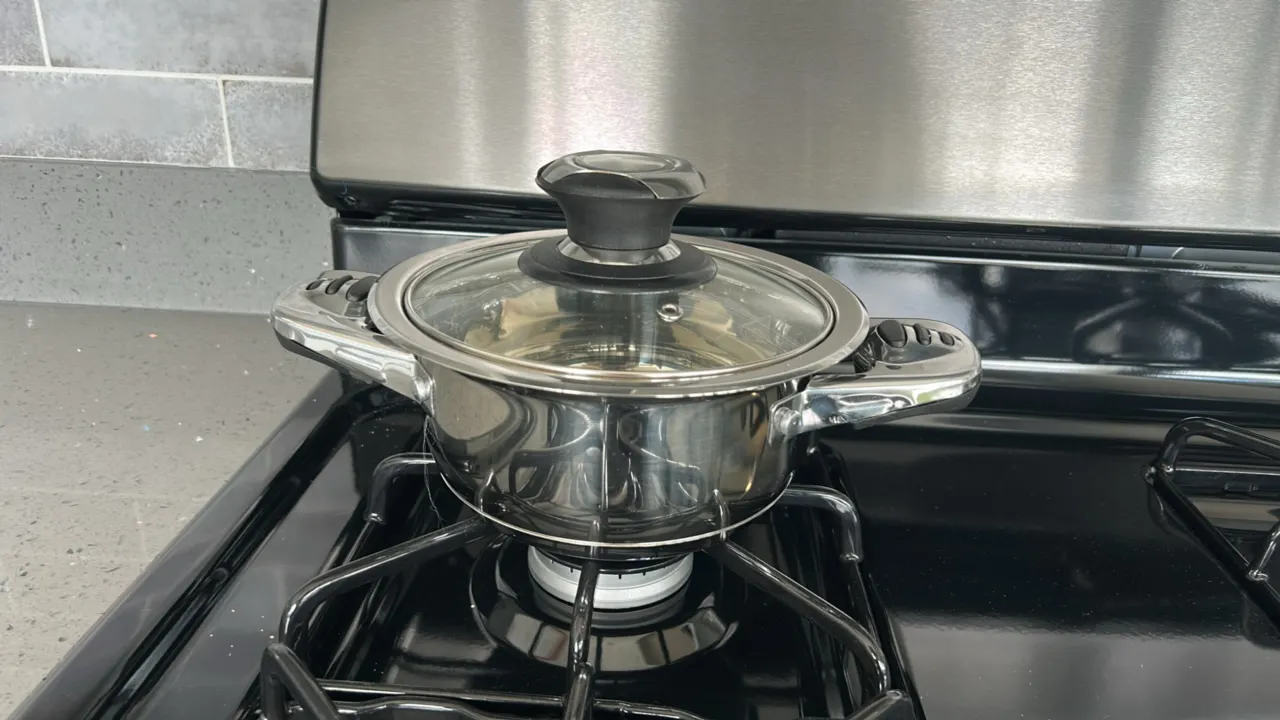 Assorted kitchen smallwares. Includes ceramic dinnerware (plates, bowls, mugs), flatware, placemats, stainless steel pot with glass lid, wire mug tree
