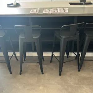 Metal barstools. Features industrial styling with matte black finish, low-profile backrests, perforated seats, integrated footrests, and tapered metal
