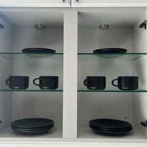 Assorted kitchen smallwares and dinnerware. Includes matte black ceramic dinner plates, side plates, and mugs; countertop utensil crock with whisk and