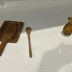 Assorted kitchenware and home decor smallwares. Includes white metal bread box, recipe tin, wooden storage box, wooden paddle board, wooden spoon, amb