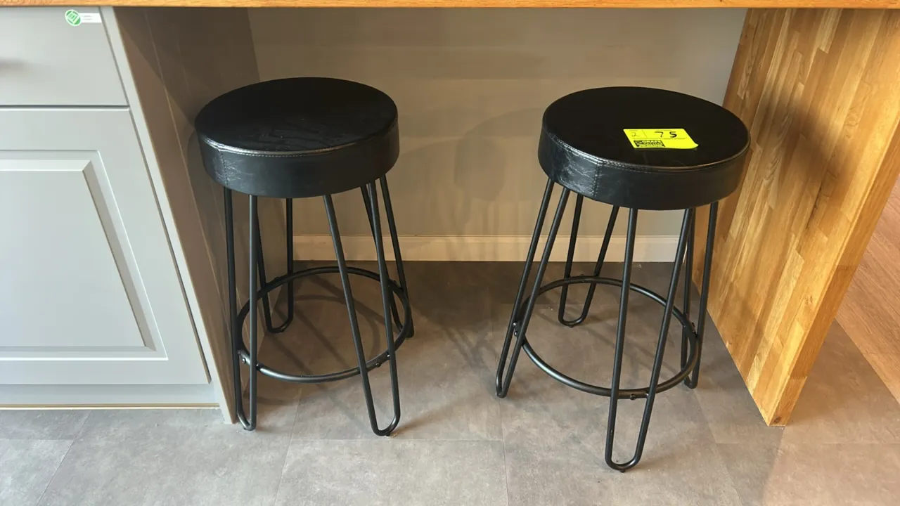 Cushioned barstools. Features round black padded seats, black metal hairpin-style legs, and integrated circular footrests. Counter and dishware not in