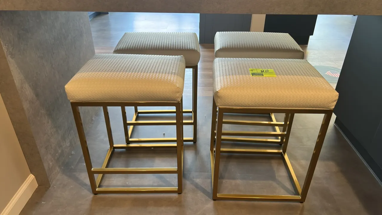 Cushioned barstools. Features off-white textured fabric upholstered seats and backless design. Mounted on gold-tone metal square frame bases with inte