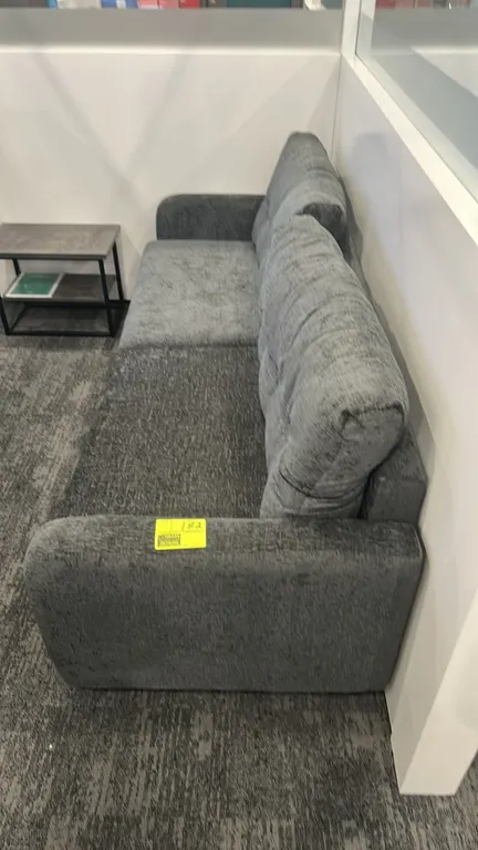 Cushioned lounge sofa. Features gray textured fabric upholstery, two tufted pillow back cushions, and low-profile metal feet. 7'L. Side table not incl
