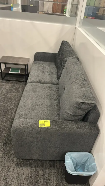 Cushioned lounge sofa. Features gray textured fabric upholstery, two-seat cushion design, button-tufted back cushions, and track arms. 7'L. Side table