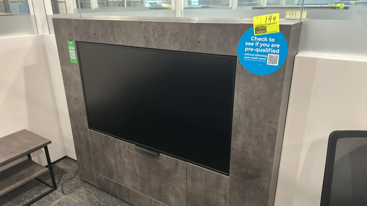 49" flatscreen built-in display monitor. Integrated into a gray faux-stone laminate media cabinet enclosure with lower access panel. Surrounding furni