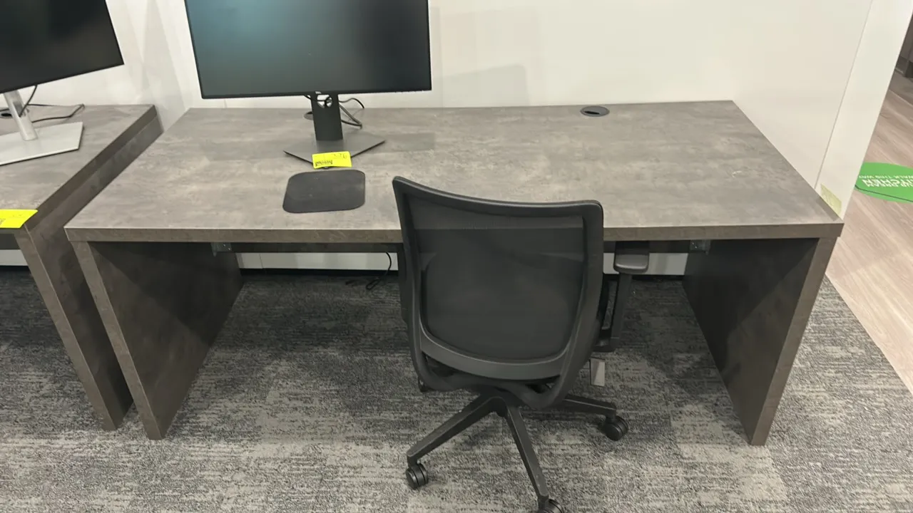 Laminate work desk with rolling office chair. Desk features a gray stone-look laminate finish, slab end panels, and desktop cable grommet. 71" x 32".
