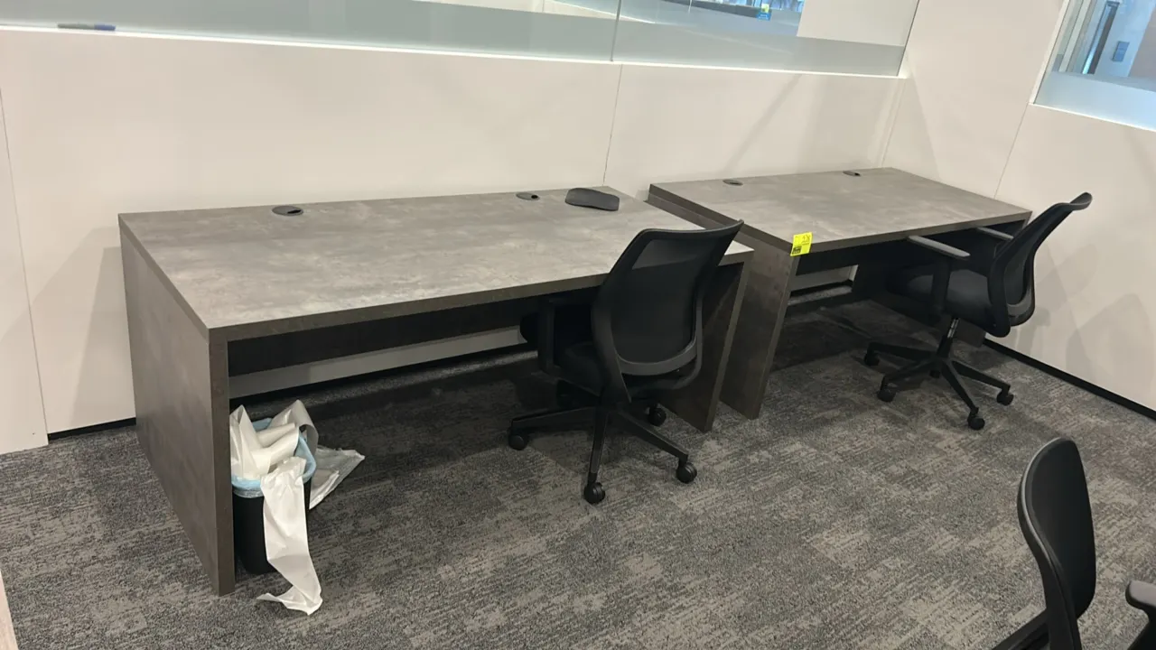 Laminate work desks with mesh office chairs. Desks feature gray stone-pattern laminate tops, dual cable grommets, and slab leg bases with modesty pane