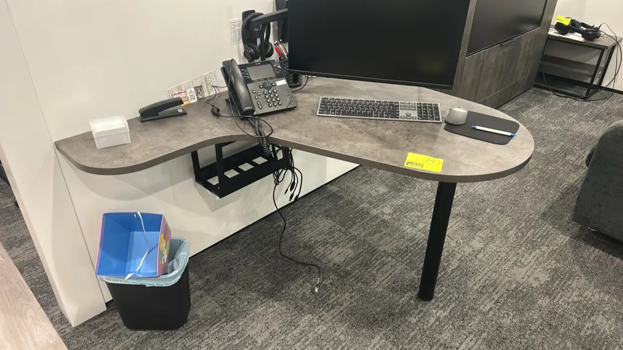 Laminate wall-mounted desk. Features a gray textured laminate top, under-desk cable management basket, and single black metal support leg. Dimensions: