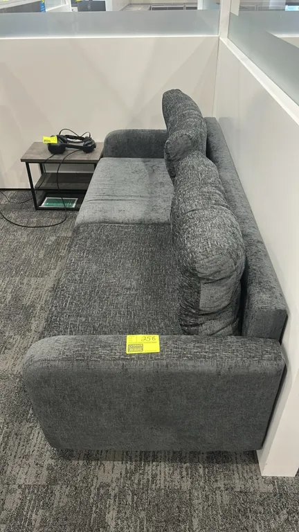 Cushioned lounge sofa. Features gray textured fabric upholstery, two seat cushions, two tufted back cushions, asymmetrical armrests, and chrome-tone f