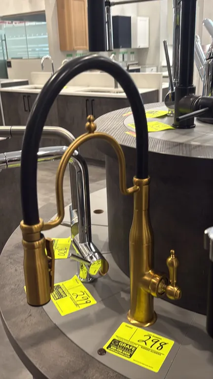 Brushed gold pull-down kitchen faucet. Features a black flexible hose, single-handle lever control, decorative support arm with finial, and pull-down