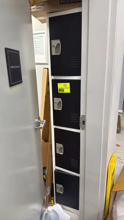 Four-tier steel employee locker unit. Features four individual compartments with louvered doors and recessed handles. Finished in white with black doo