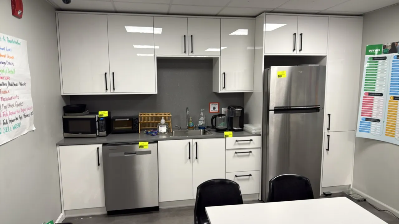 Breakroom kitchen cabinet unit with countertop and sink. Features white gloss cabinetry with black pulls, gray countertop, stainless steel sink with f