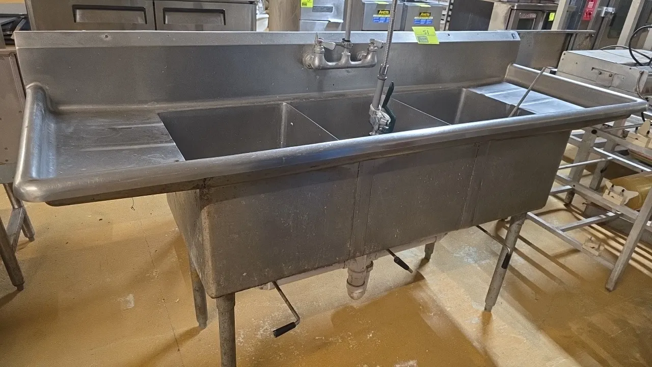 Stainless steel 3-compartment sink. Features left and right drainboards, integrated backsplash, splash-mount faucet with pre-rinse sprayer, and lever