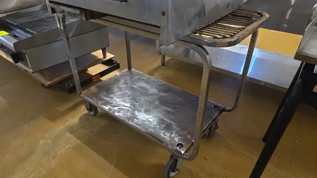 Metal 2-tier stock cart. Features a slatted upper tier, solid bottom shelf, and tubular metal frame. 37". Mounted on casters. Contents not included.