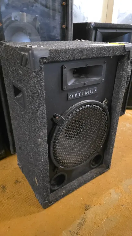 Optimus 40-0120 12" PA speaker. Features carpeted enclosure, protective corner guards, recessed side carry handles, horn tweeter, 12" woofer with prot