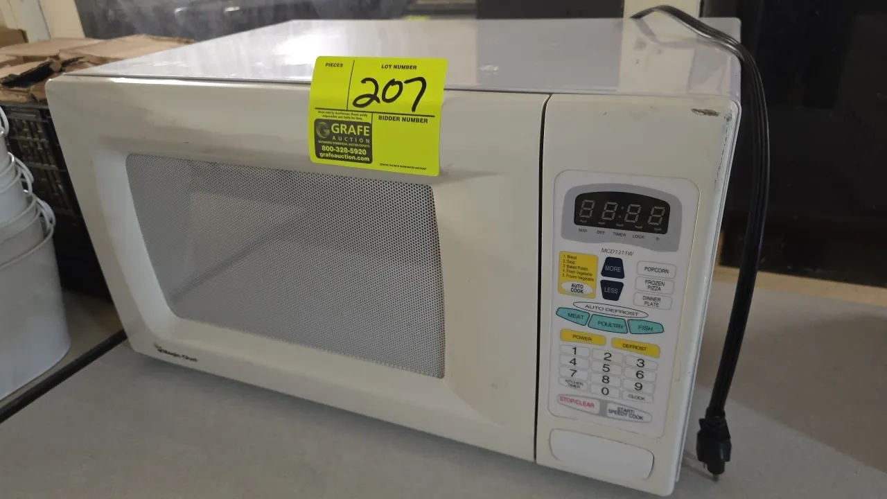 2007 Magic Chef MCD1311W countertop microwave oven. Features digital touchpad controls, push-button door release, and interior glass turntable. S/N: 7