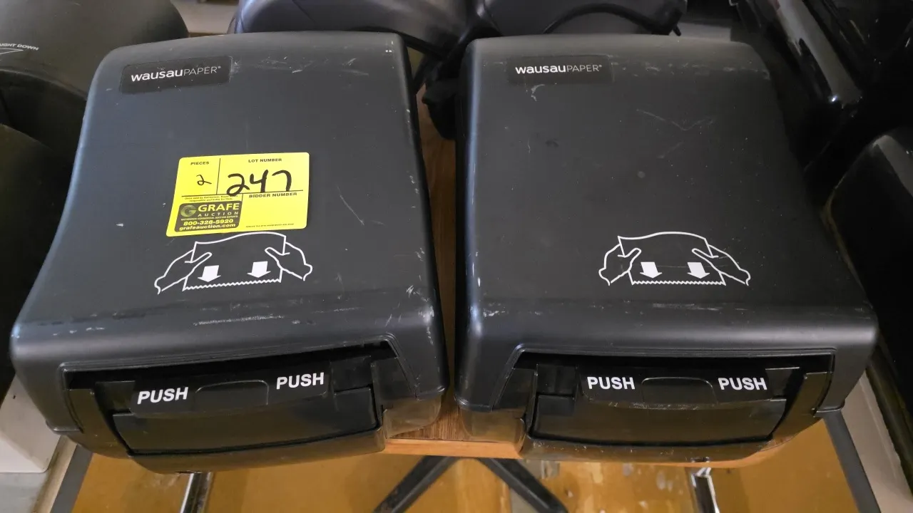 Wausau Paper manual paper towel dispensers. Features black plastic housing, manual push bar dispensing mechanism, and instructional graphics. Designed