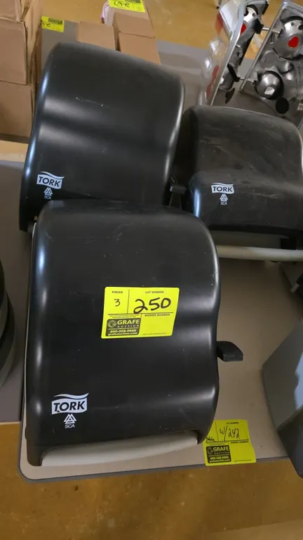 Tork manual paper towel dispensers. Features black plastic housing, side lever manual dispensing mechanism, and roll towel capacity. Designed for wall