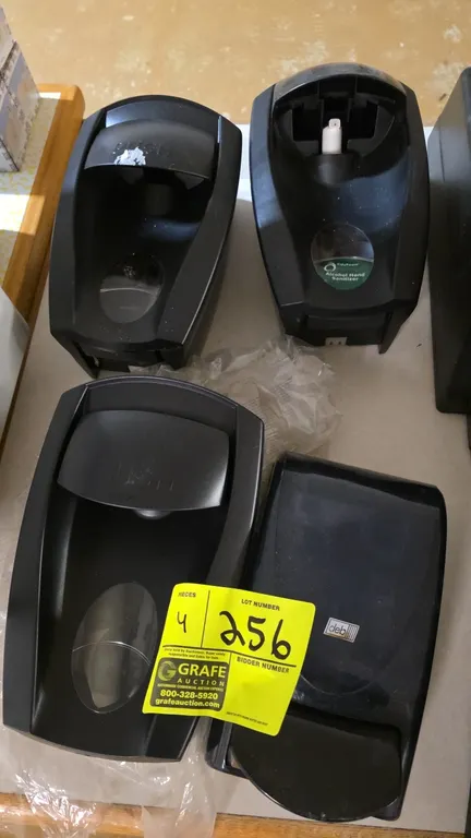 Assorted manual soap and sanitizer dispensers. Features black plastic construction and manual push-bar operation. Includes Deb and TidyFoam units. Uni