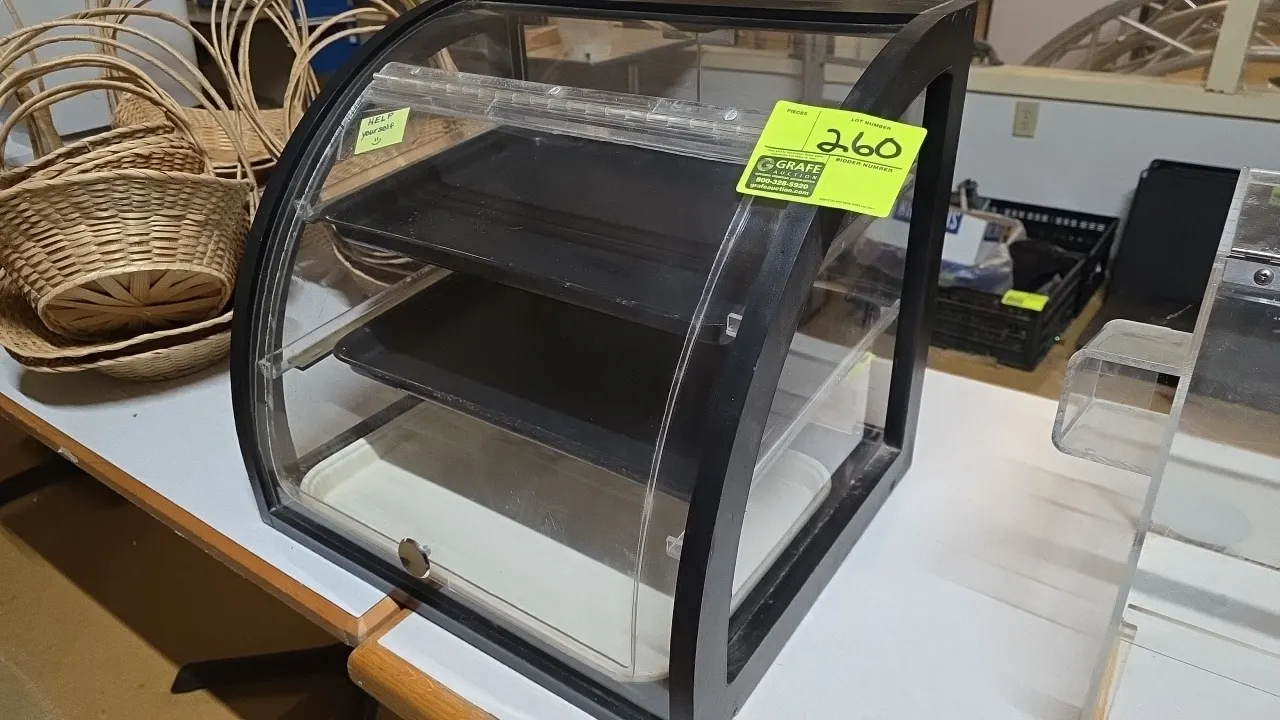 Countertop bakery display case. Features a black laminated wood frame, clear acrylic panels, curved front flip-up door, dual rear hinged access doors,