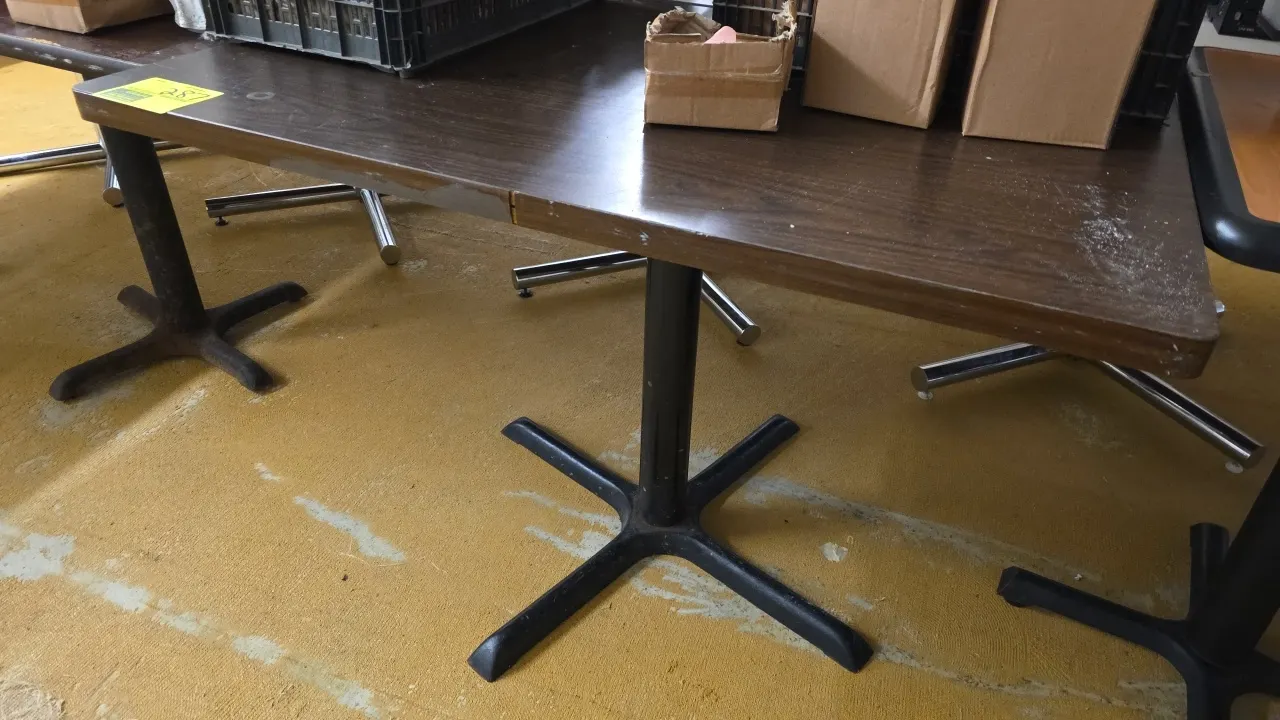 Laminate dining table. Features a dark woodgrain finish top. 42" x 30". Mounted on a black metal cross pedestal base. Note: Section of edge banding is